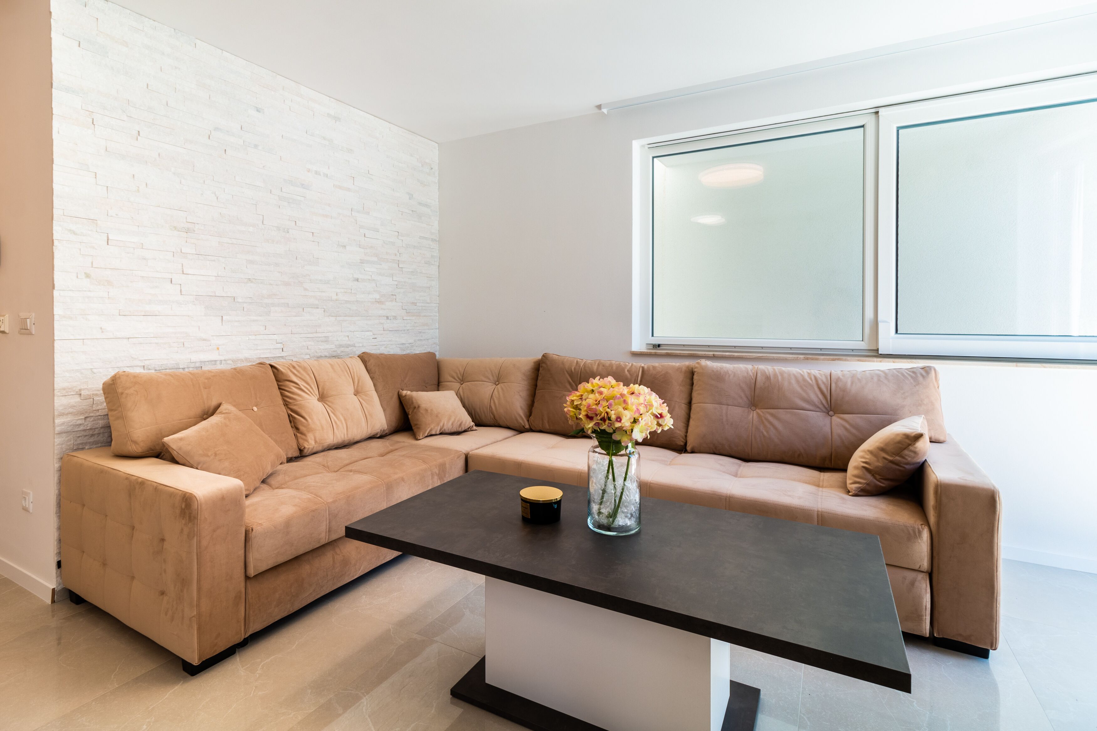 A modern living room with a sectional sofa, a coffee table, and a vase with flowers.