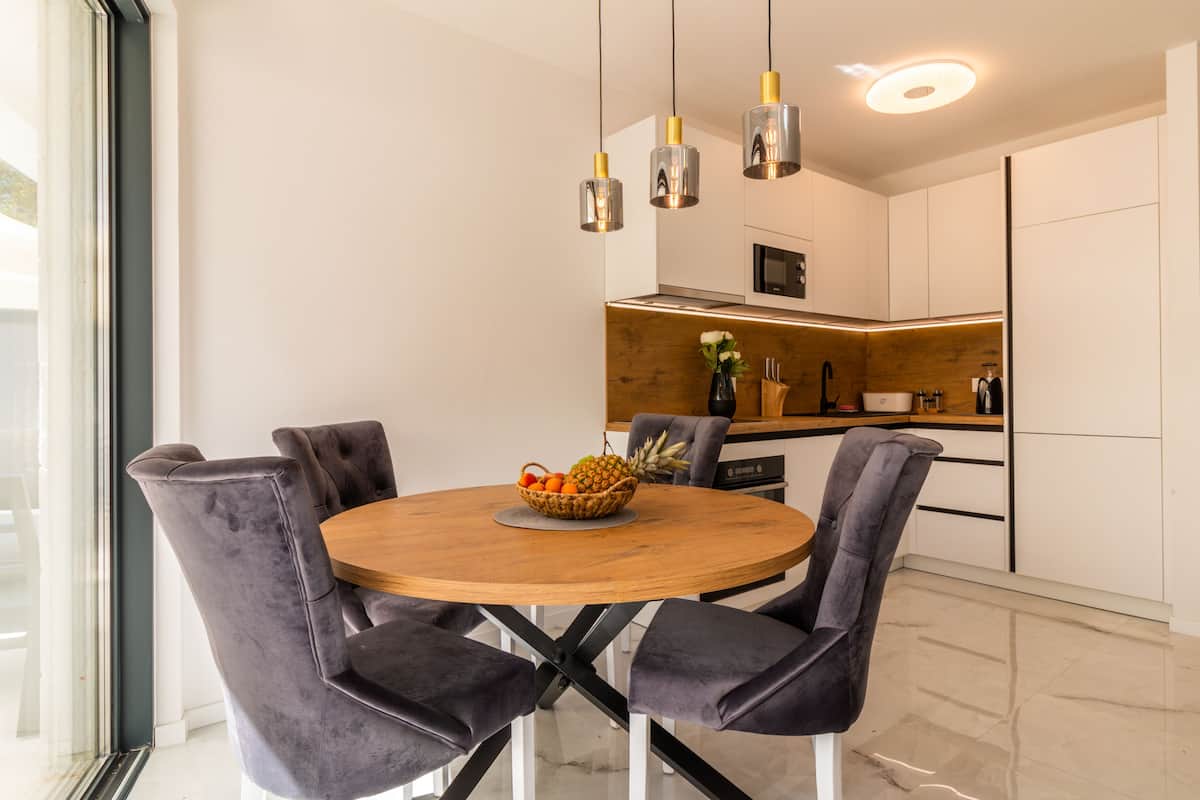 A modern dining area with a round wooden table, grey upholstered chairs, and pendant lighting.