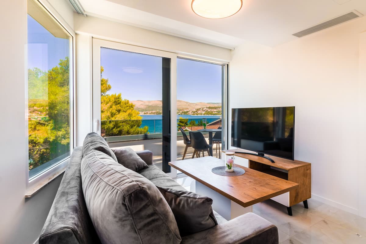 A modern living room with a large window, a sofa, a wooden coffee table, and a TV.