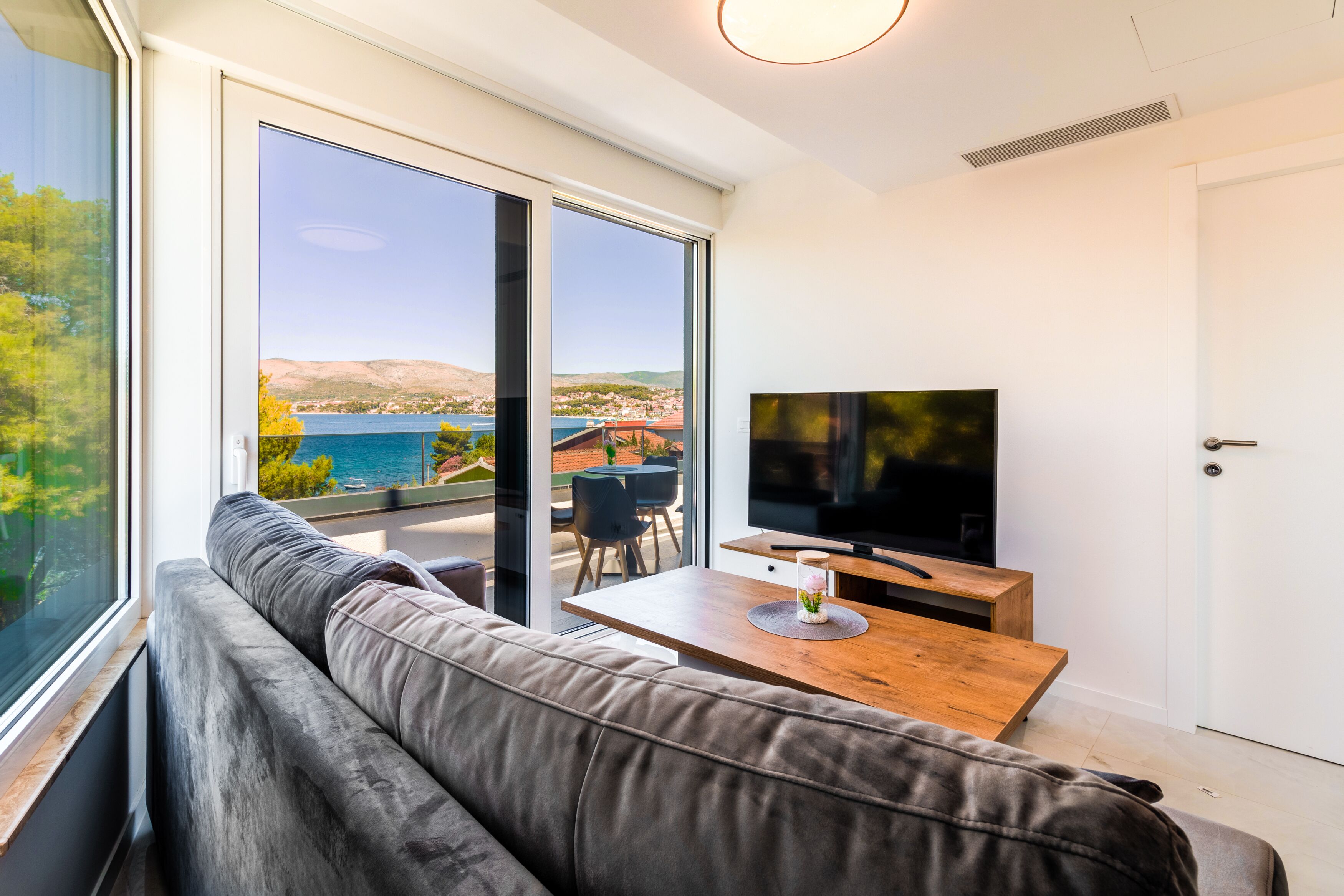 A modern living room with a large window, a sofa, a wooden table, and a television.