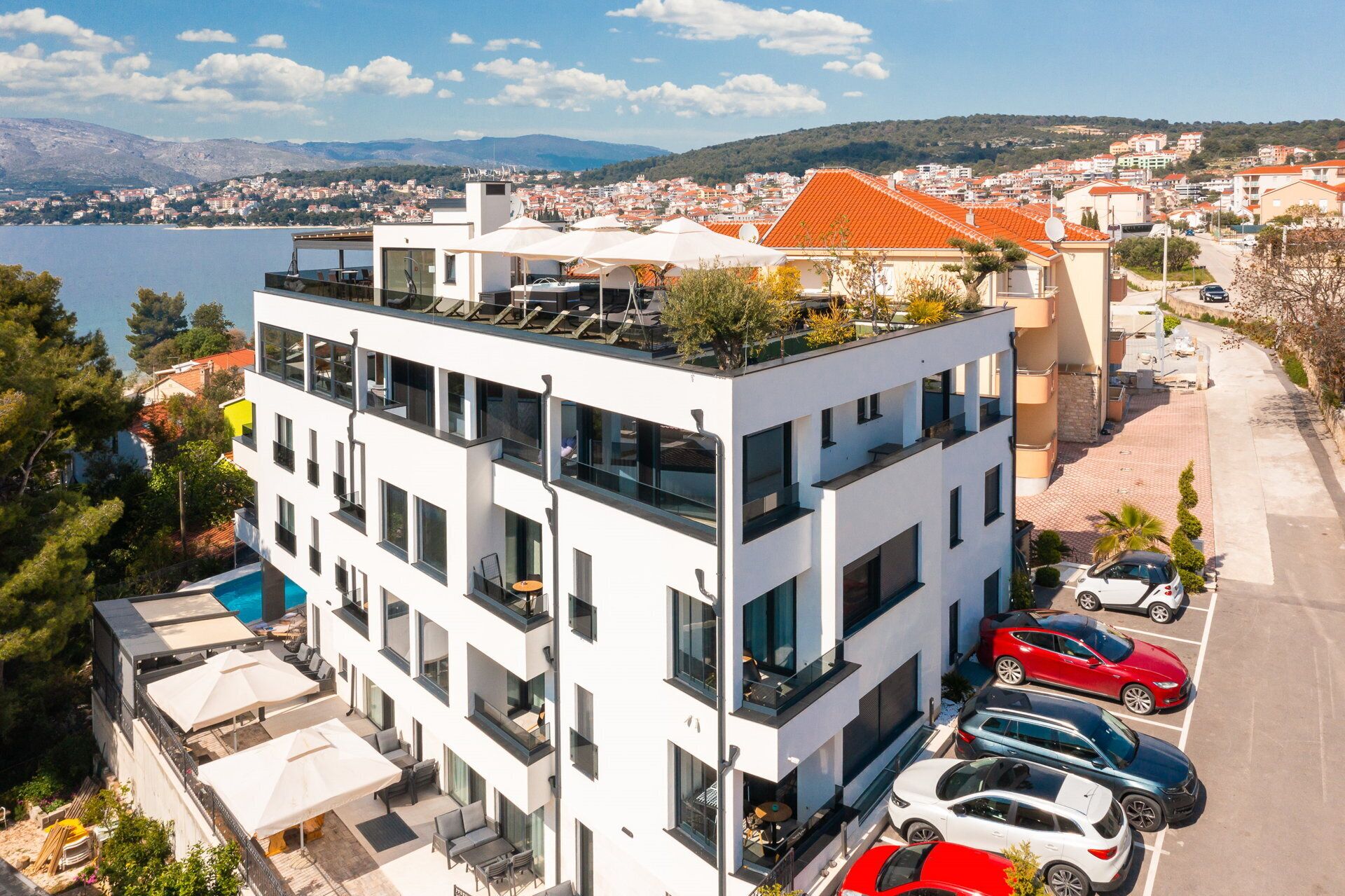A modern multi-story hotel with balconies, a rooftop garden, and a view of the sea and town.