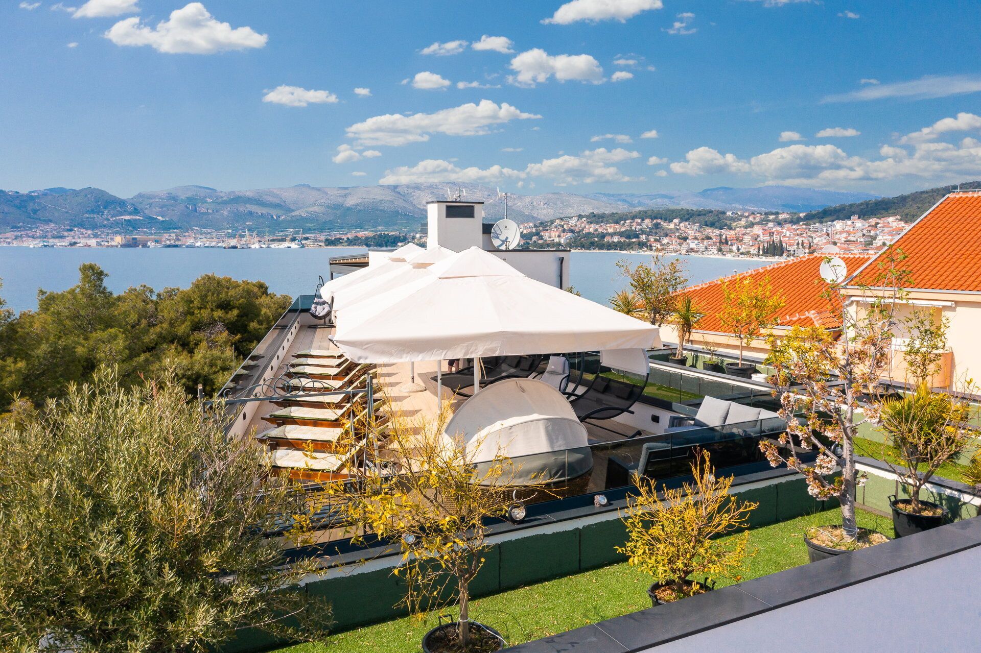 Une terrasse sur le toit, agrémentée d’un parasol blanc, de sièges d’extérieur et offrant une vue sur un lac et le paysage urbain.