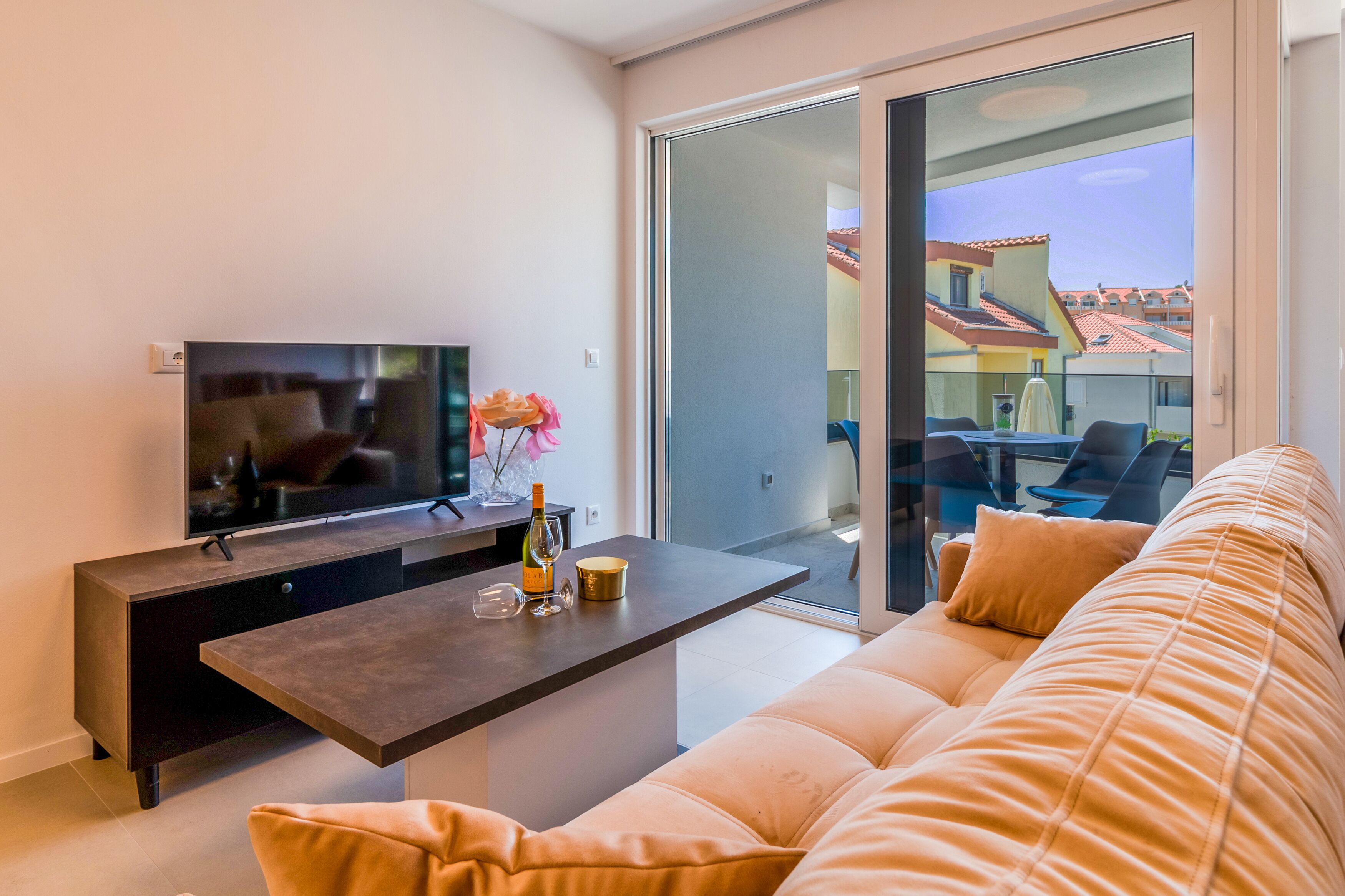 Een moderne woonkamer met een flatscreen-tv, een donker houten salontafel, een beige bank en een balkon met een glazen deur.