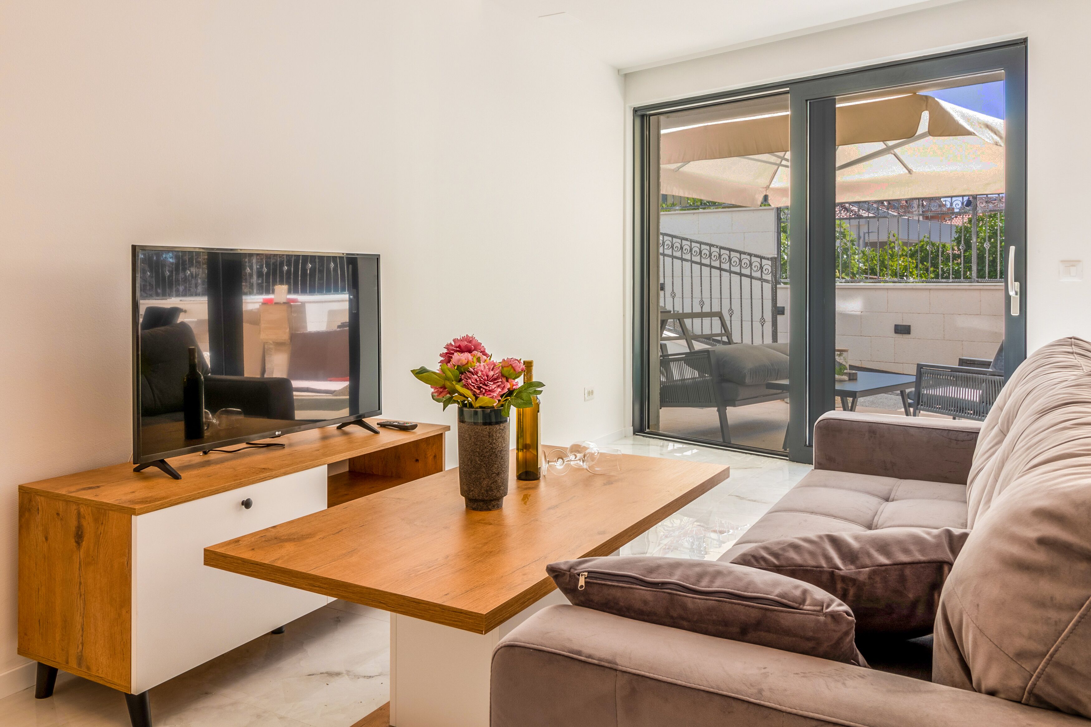 Een moderne woonkamer met een houten bureau, een flatscreen televisie, een bank en een glazen schuifdeur naar een terras.