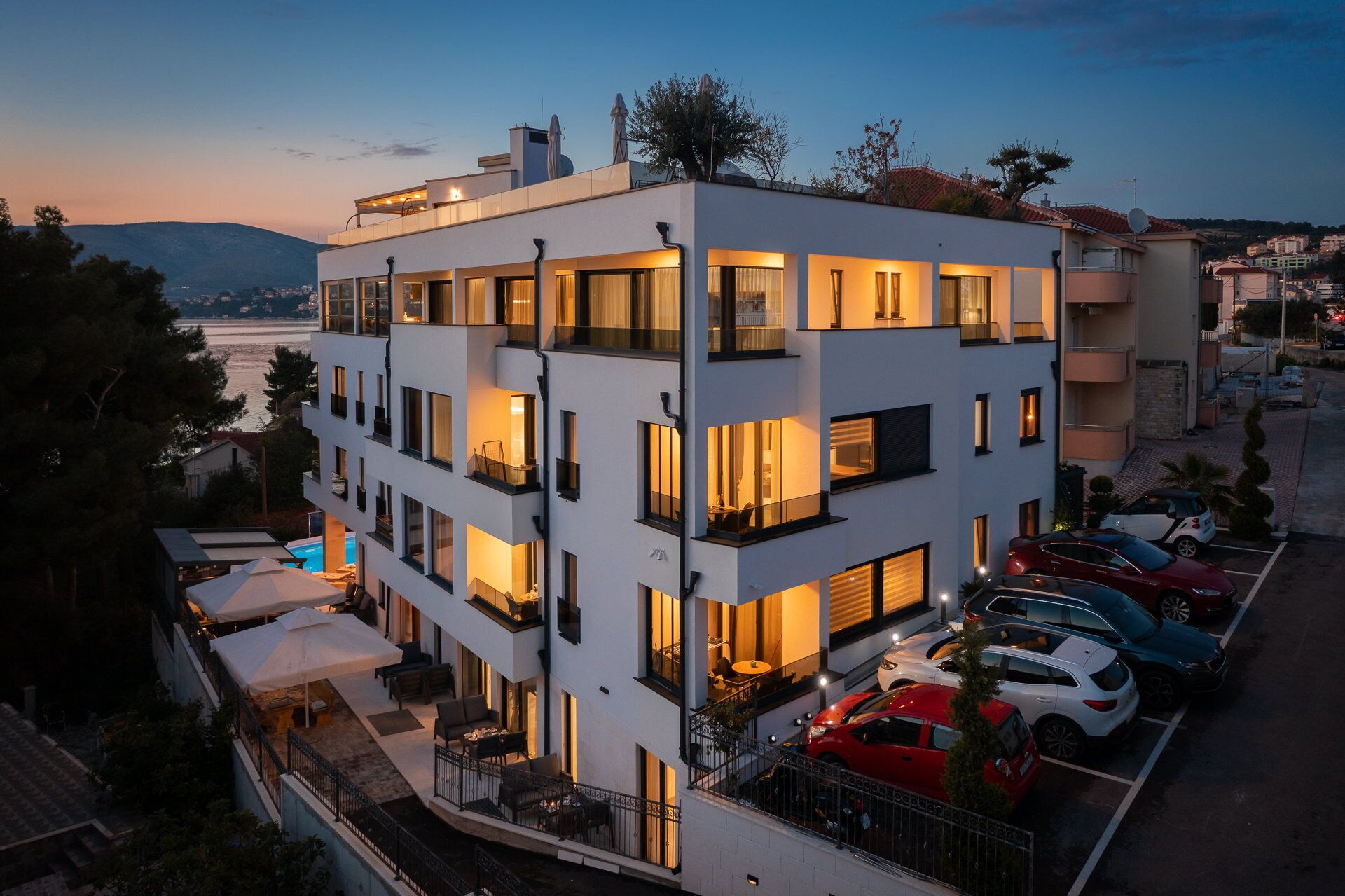 Un edificio de varios pisos con balcones, una piscina y un estacionamiento con varios coches.