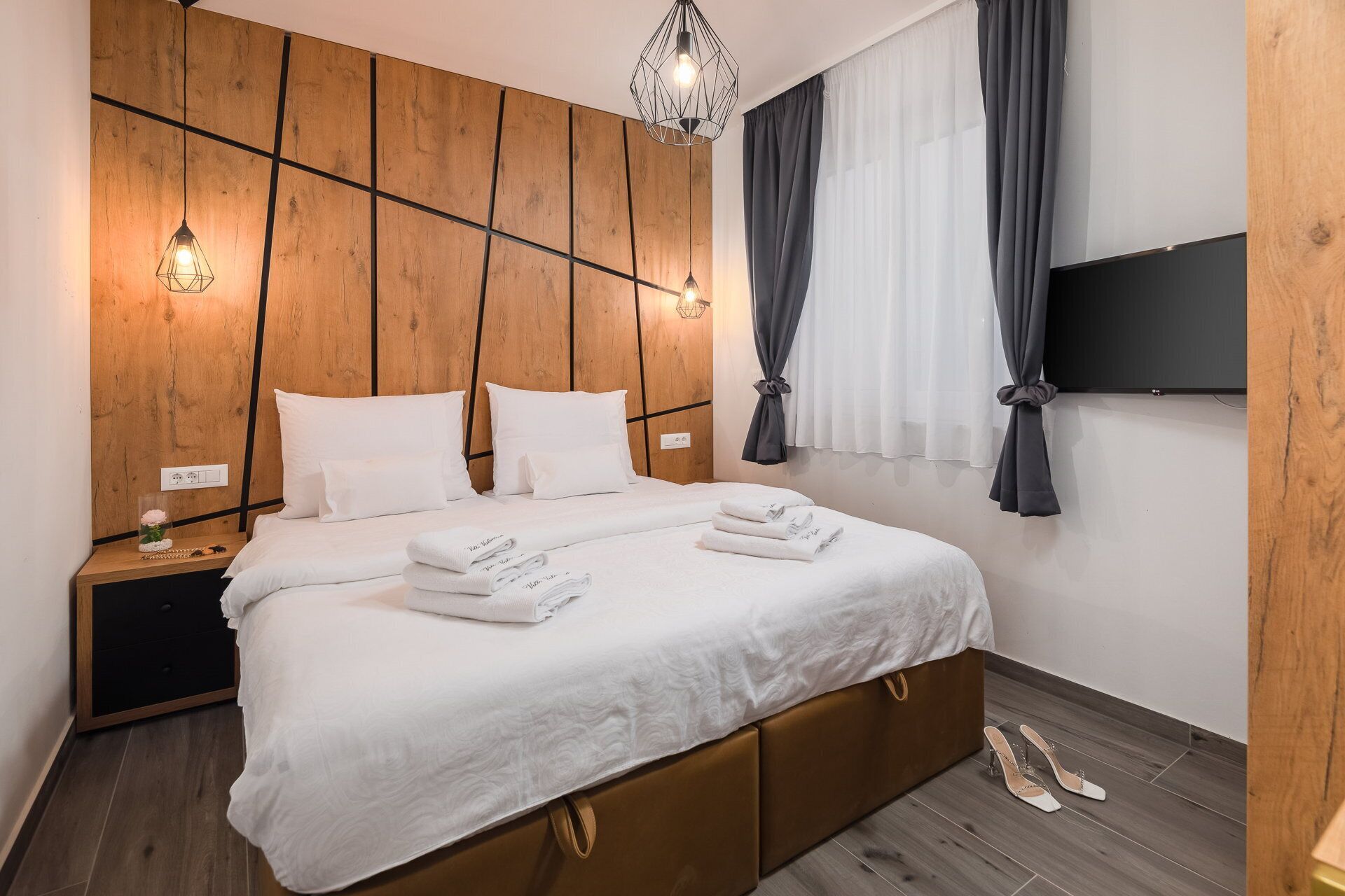 Een moderne hotelkamer met een houten hoofdbord, een groot bed met witte lakens, een nachtkastje met een lamp en een aan de muur bevestigde televisie.