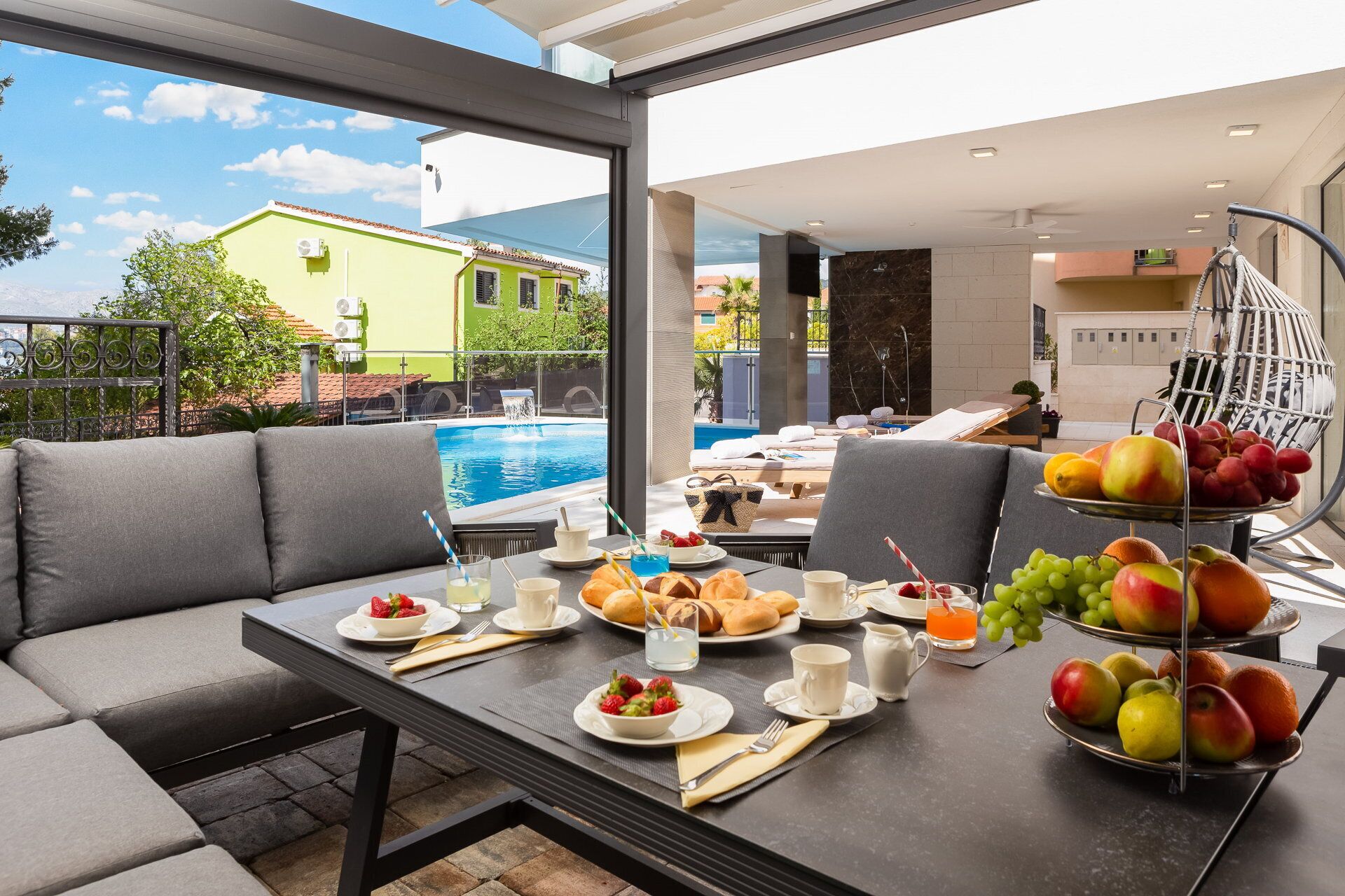 Un espace repas avec vue sur la piscine, des sièges en plein air et un présentoir de fruits.