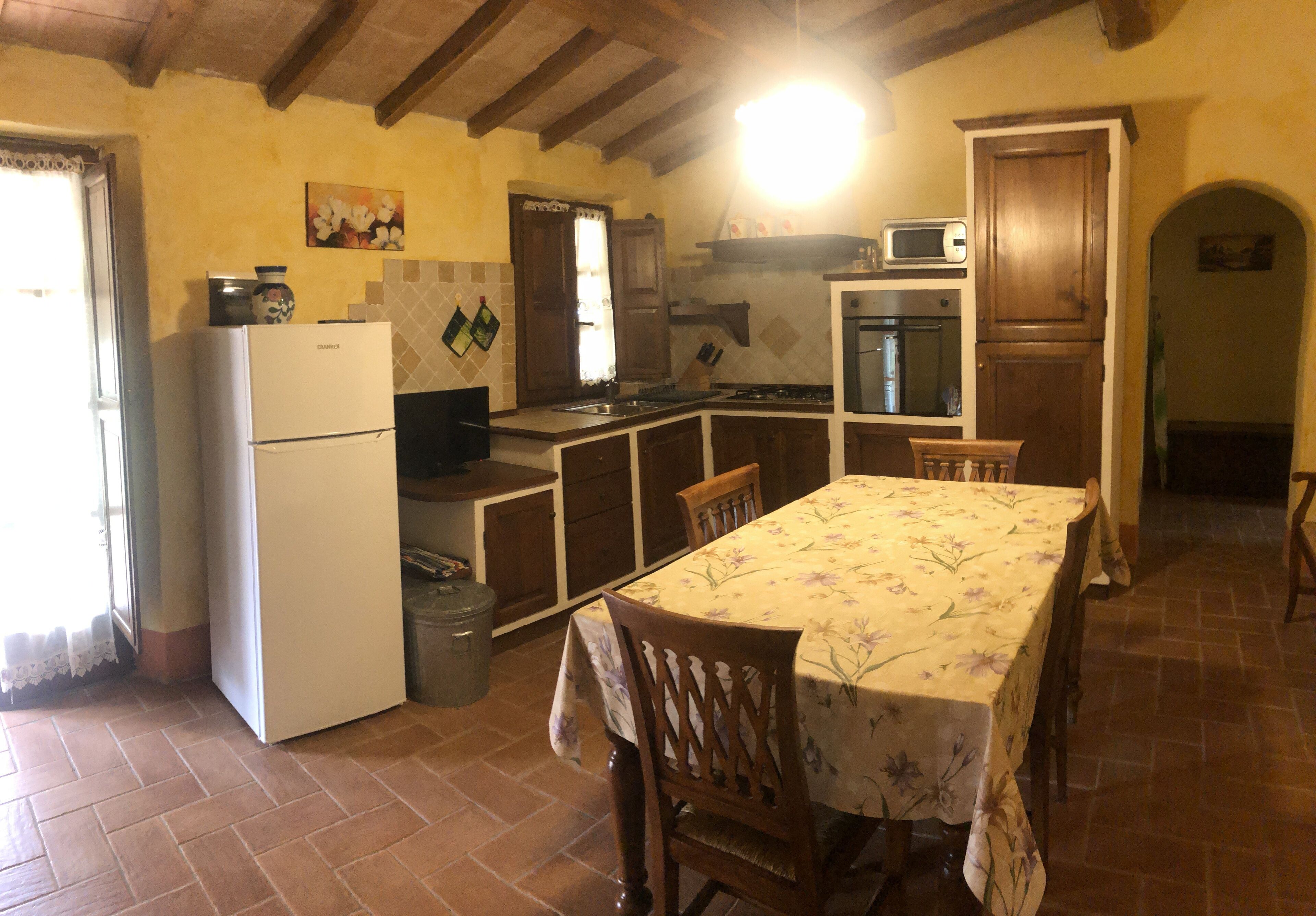 Una cucina con frigorifero, fornello, microonde e pensili in legno. C'è un tavolo da pranzo con sedie e una finestra con tende.