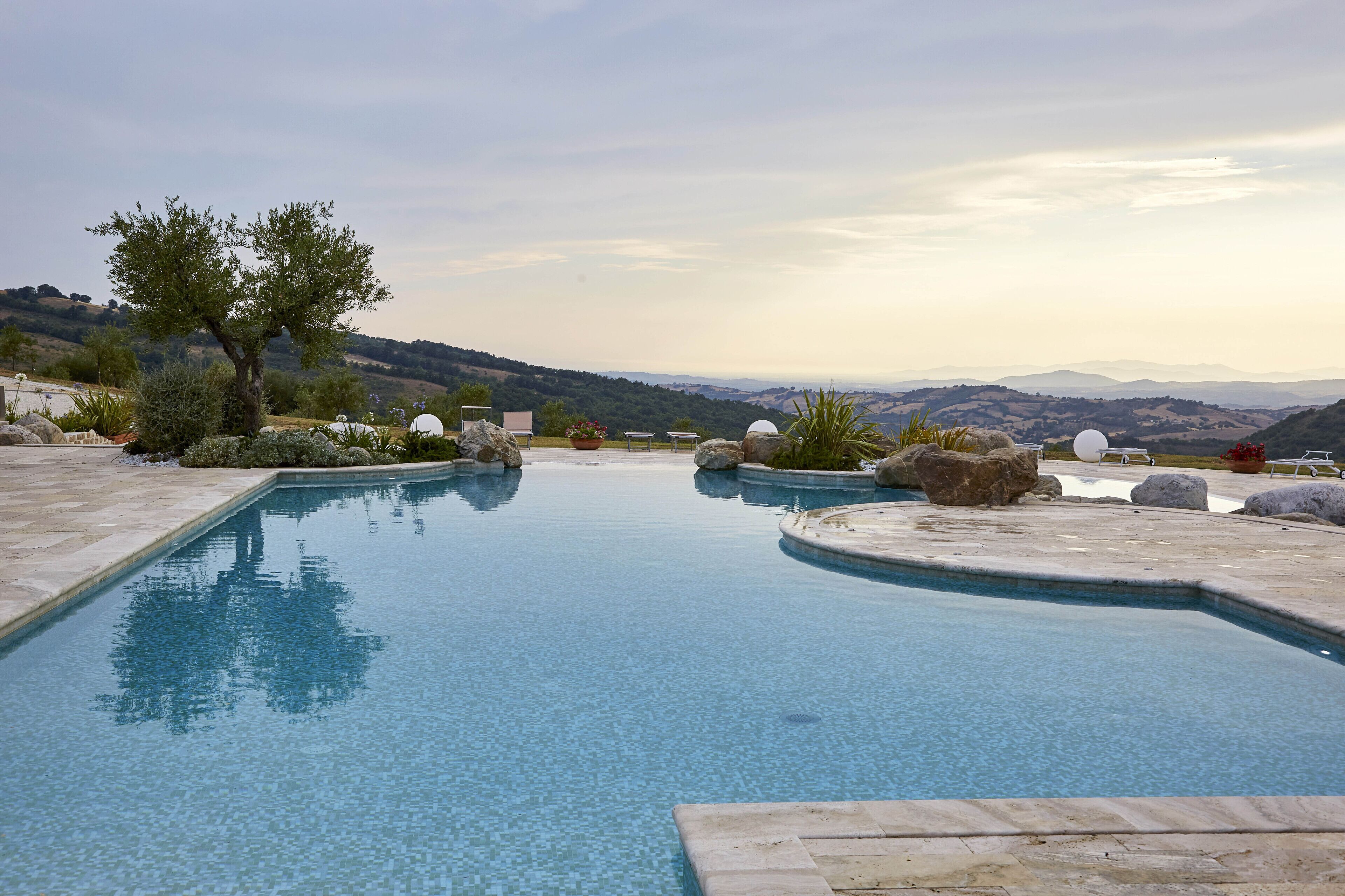 A swimming pool with a view of distant hills, surrounded by rocks and plants.