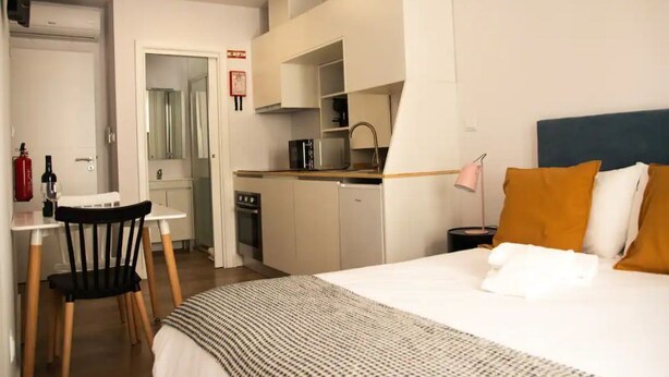 Et kompakt hotelværelse med seng, skrivebord, stol, tekøkken og badeværelse.