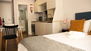 Et hotelværelse med seng, lille tekøkken, spiseplads med stol og bord, og badeværelse, der kan ses igennem en åben dør.