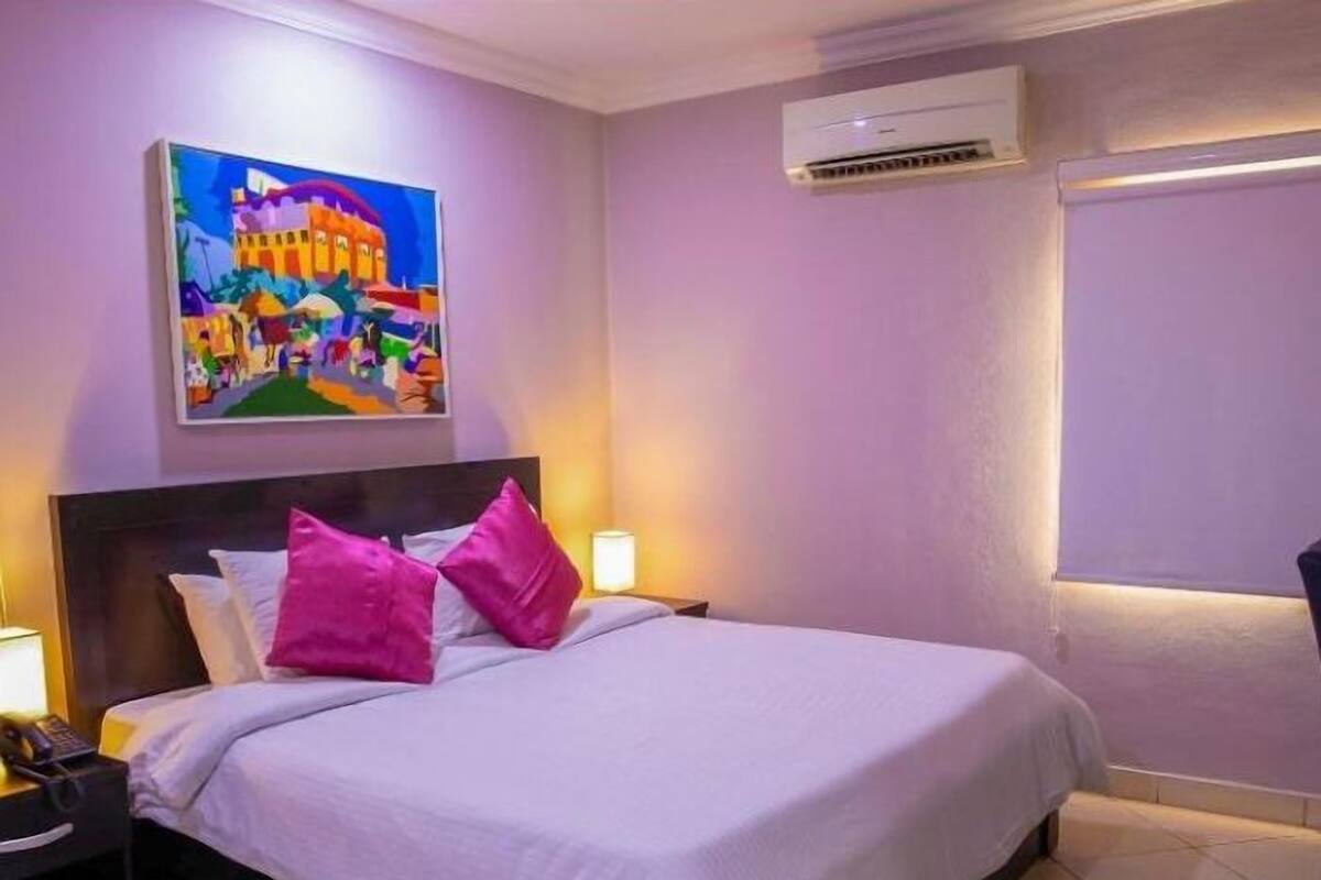 Habitación de hotel con cama, dos mesitas de noche, aire acondicionado y un cuadro en la pared.