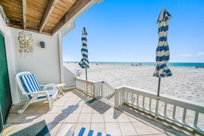 Une véranda donnant sur la plage, avec deux parasols rayés, une chaise blanche et une vue sur la plage.