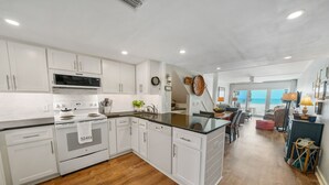 A modern kitchen with white cabinetry, a central island, and a view to the beach. - Very Merry - Renovated Gulf-Front Escape, Steps To Beach (Panama City Beach)