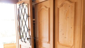 Ein Holzkleiderschrank mit einer Tür im Rautenmuster, ein rot gemusterter Teppich und eine Holzbank davor.