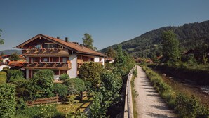 Eine zweistöckige Chalet mit Balkon, umgeben von üppiger Vegetation und einem Fluss.