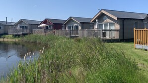 A row of mobile homes with a wooden deck and a pond in the foreground. - The Lake House -  a meadow lodge that sleeps 4 guests  in 2 bedrooms (Filey)