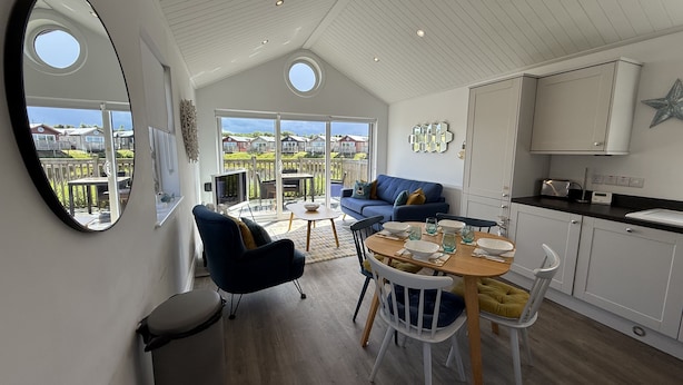 A modern kitchen with white cabinets, a dining area with a round table, and a blue sofa. - The Lake House -  a meadow lodge that sleeps 4 guests  in 2 bedrooms (Filey)