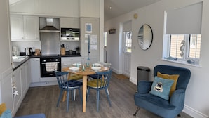 A compact kitchen with white cabinets, a stove, and a dining area with blue chairs and a wooden table. - The Lake House -  a meadow lodge that sleeps 4 guests  in 2 bedrooms (Filey)