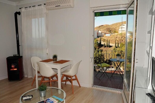 A modern living room with a dining area, a fireplace, and a balcony with a view of a hilly landscape.