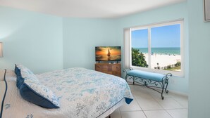 A bedroom with a bed, a bench, a TV, and a window with a beach view. - 🌴 Caprice Resort Unit #201 – Corner Gulf Front Condo with Water Views (Saint Pete Beach)