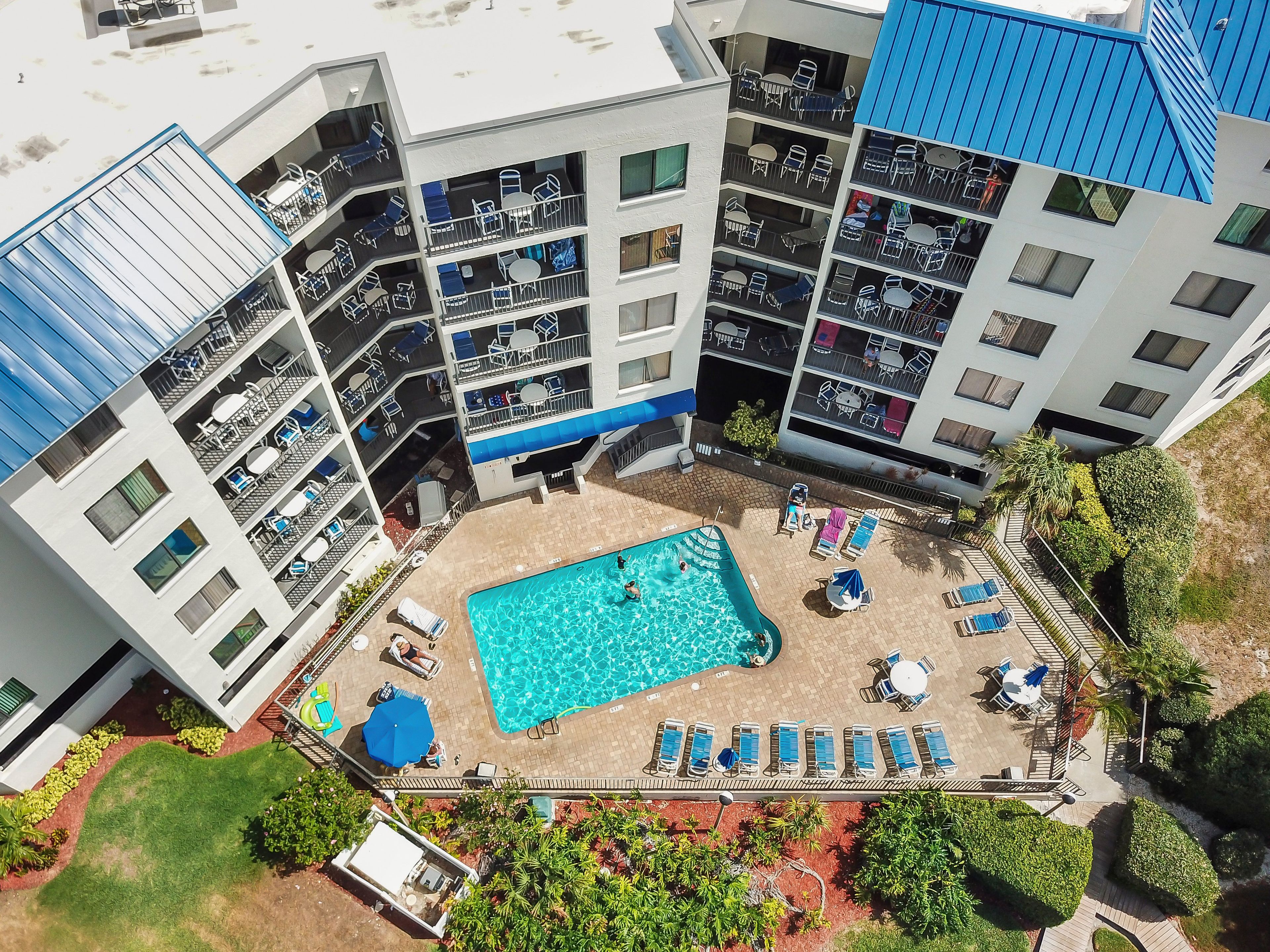 A multi-story building with a rooftop pool area, outdoor seating, and a landscaped garden.