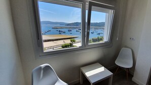 A room with a large window overlooking a marina with boats. There is a small table and two chairs. - Estudio Vista Mar Muxia (Muxía)