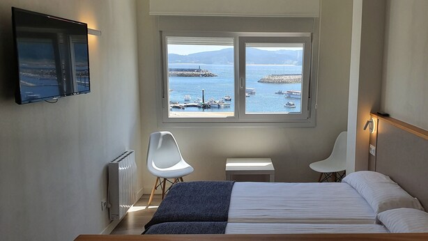 A bedroom with a bed, a desk, a chair, and a TV mounted on the wall. - Estudio Vista Mar Muxia (Muxía)