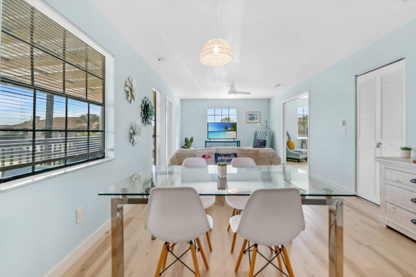 A modern dining area with a glass table and chairs, a ceiling fan, and a view of the outdoors.