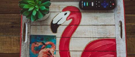 A wooden tray with a red flamingo, a remote control, and a small painting.