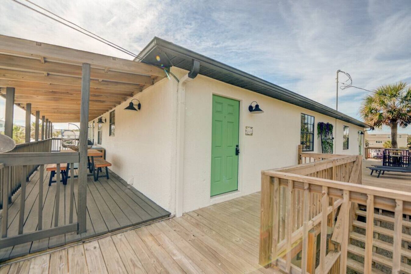Une terrasse en bois avec des sièges d’extérieur, une porte verte et un espace abrité avec des tables et des chaises.