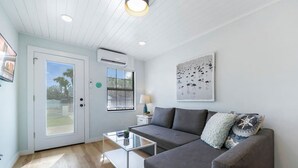 Een moderne woonkamer met een grijze bank, een glazen salontafel en een witte deur die leidt naar een balkon.