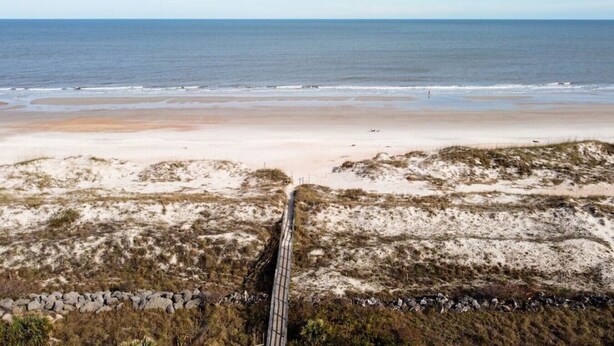 Een kustweg die naar een strand leidt, met duinen en een helder uitzicht op de oceaan.
