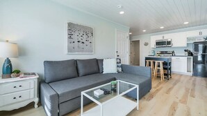 Een moderne woonkamer met een grijze bank, een salontafel en een keuken met witte kasten en roestvrijstalen apparatuur.