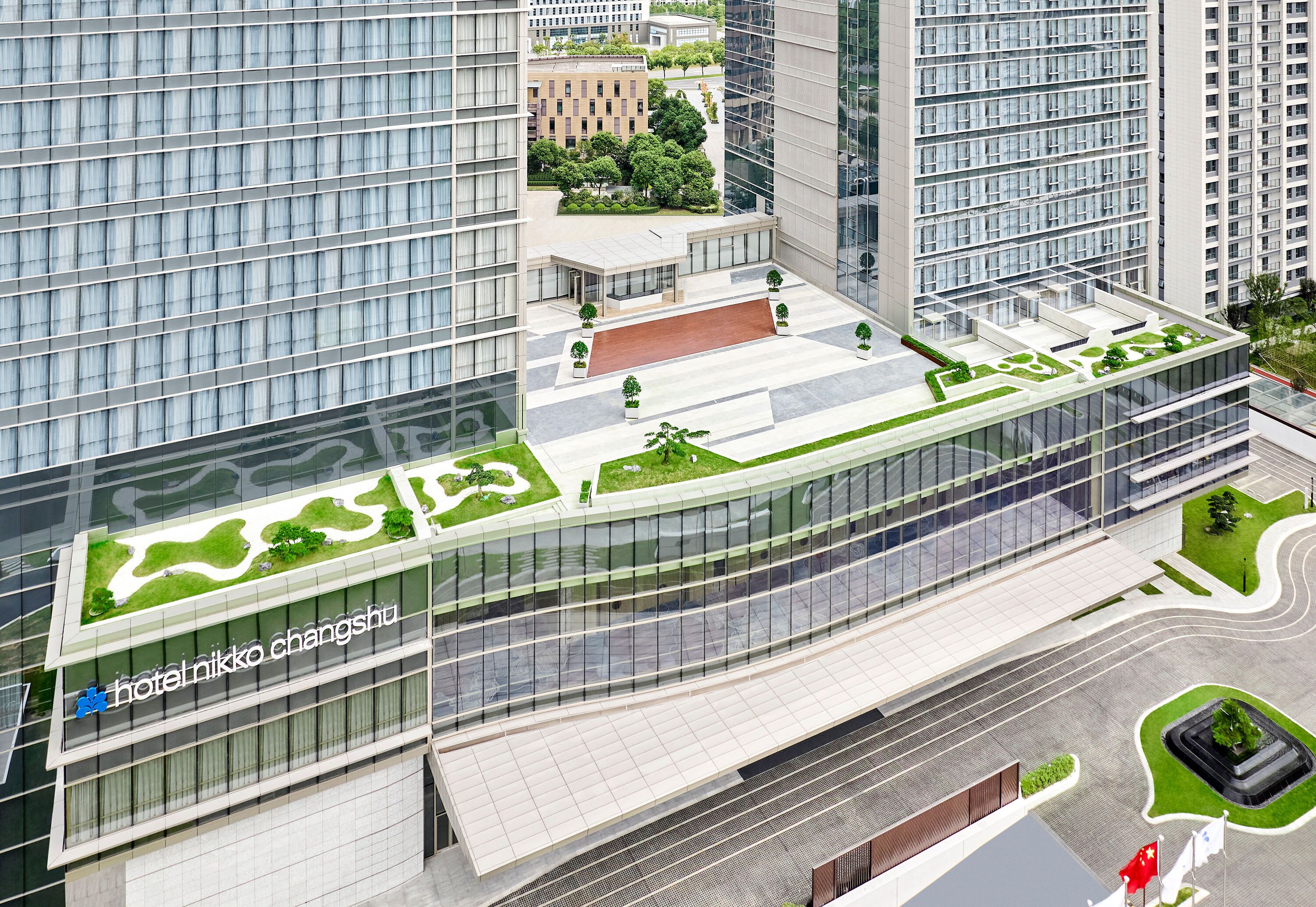 Un hotel moderno con fachada de vidrio, jardín en la azotea y un amplio vestíbulo.