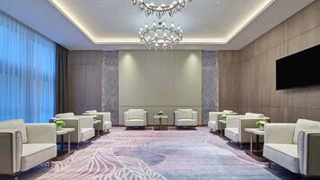 A modern hotel lobby with a large chandelier, seating area, and a flat-screen TV on the wall.