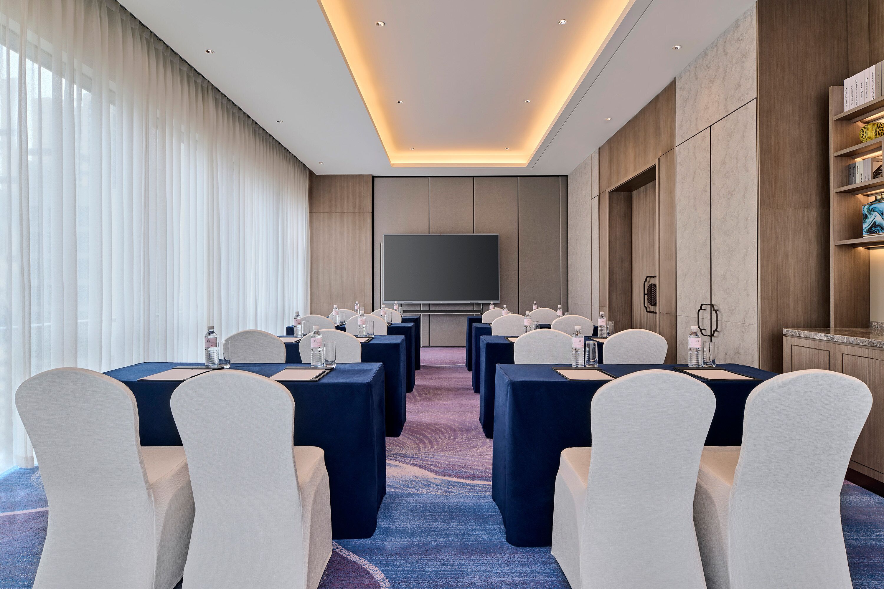 A conference room with a large flat-screen TV, white chairs, and tables set up for meetings.