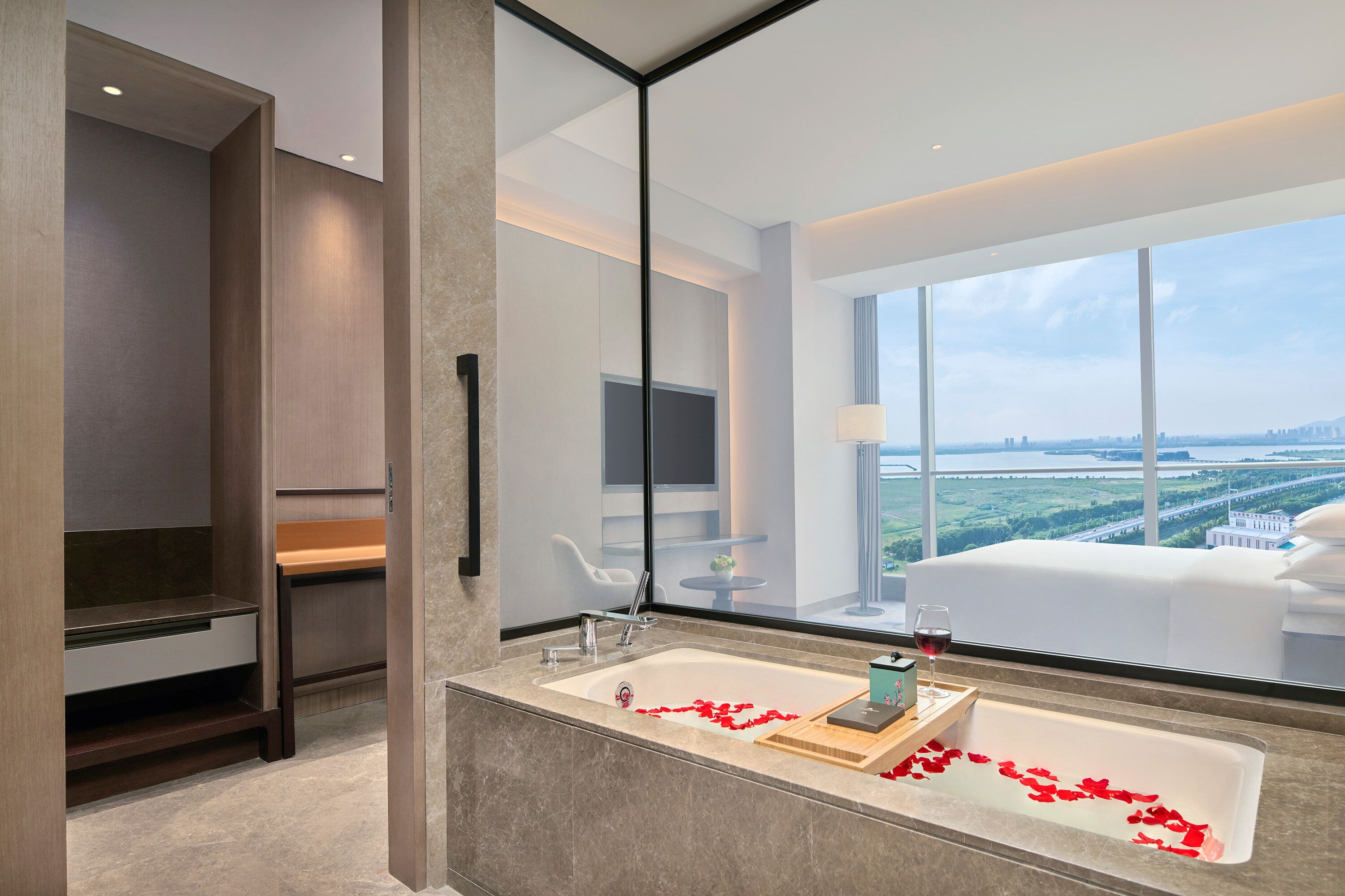 A modern bathroom with a large window, a bathtub with rose petals, and a view of a cityscape.