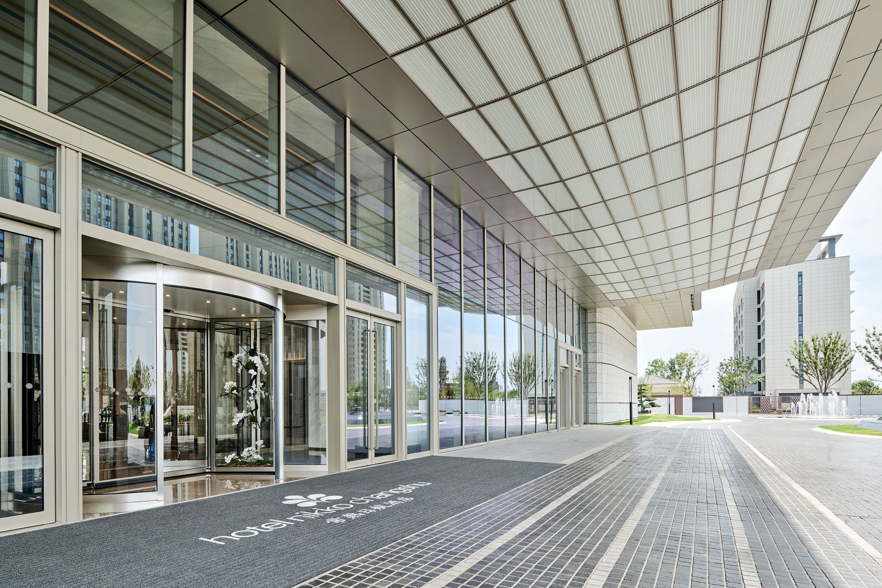 A modern hotel entrance with a glass facade, a covered walkway, and a clear view of the parking area.