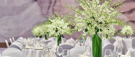 Una mesa de banquete decorada con manteles blancos, cristalería y un gran centro de mesa floral blanco.