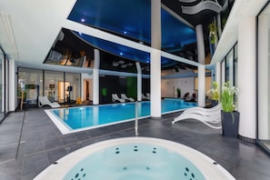 Una piscina interna con idromassaggio, sedie a sdraio e un moderno design del soffitto.