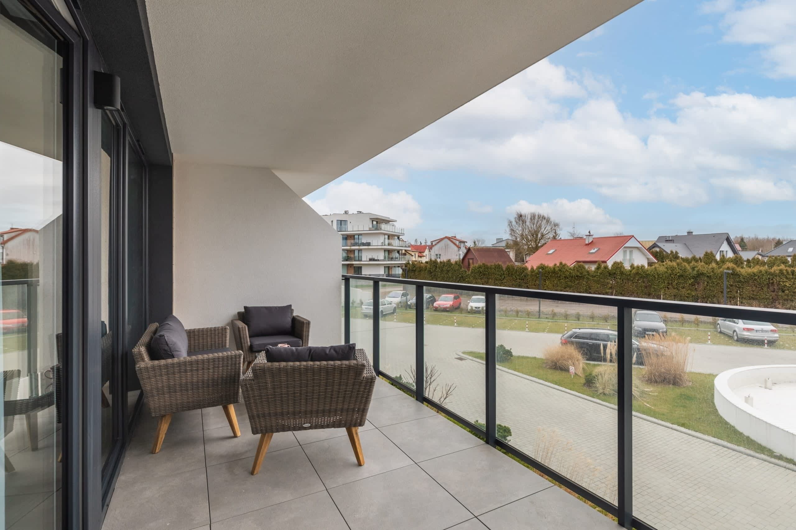 A balcony with wicker furniture, a glass door, and a view of parked cars and houses.