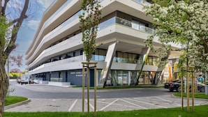 Ein modernes, mehrgeschossiges Gebäude mit einer gewölbten Fassade, einem Parkplatz und einem Schild für eine Klinik für altersbedingte Beschwerden.