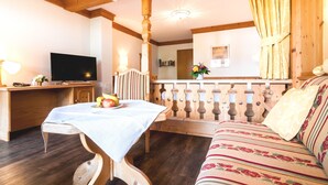 Um quarto aconchegante com teto de madeira, uma televisão sobre um móvel de madeira, uma mesa de jantar com toalha branca e um sofá com estofamento floral.