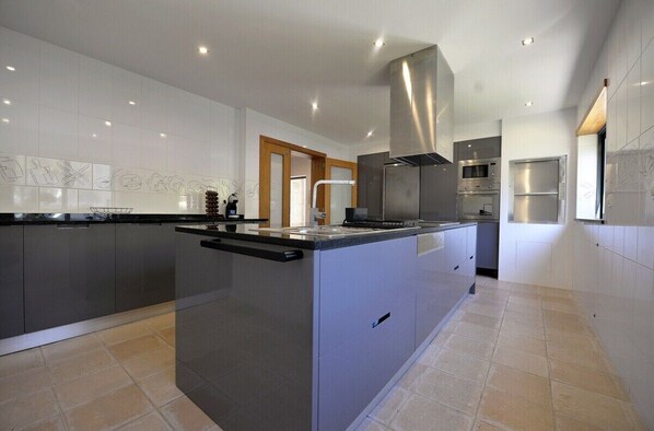A modern kitchen with stainless steel appliances, a central island, and a large window providing natural light. - Villa 298 Holiday Villa w/ Sea and Mountain Views (Caminha)