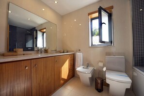 A modern bathroom with a wooden vanity, a large mirror, a toilet, and a window.