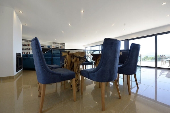 A modern dining area with blue upholstered chairs, a wooden table, and a view of the outdoors through large windows.