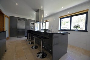 A modern kitchen with a central island, bar stools, and a large window providing natural light. - Villa 298 Holiday Villa w/ Sea and Mountain Views (Caminha)