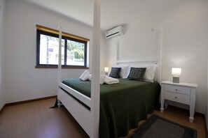 A bedroom with a bed, a nightstand, an air conditioning unit, and a window.