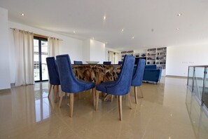A modern dining area with a wooden table and blue chairs, a glass railing, and a bookshelf in the background.